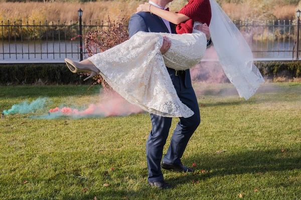 Bruidegom houdt de bruid in zijn armen tegen de achtergrond van rook — Stockfoto