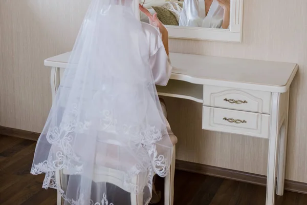 Bruden sitter nära bordet i rummet i en badrock — Stockfoto