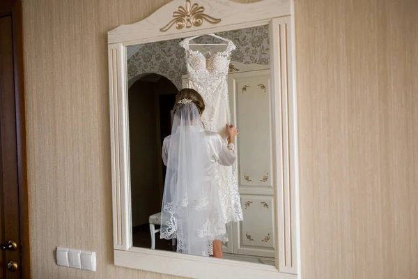 Невеста в халате с свадебным платьем в руках — стоковое фото