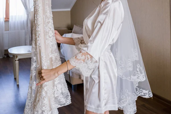 バスローブ姿で花嫁がウェディング ドレスのそばに立つ — ストック写真