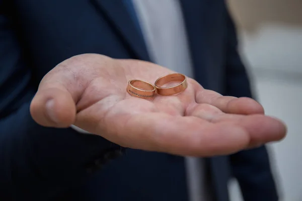 Novio sostiene anillos de boda en su mano —  Fotos de Stock