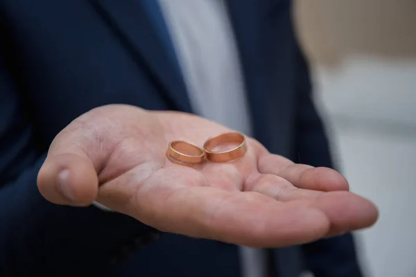 Novio sostiene anillos de boda en su mano — Foto de Stock