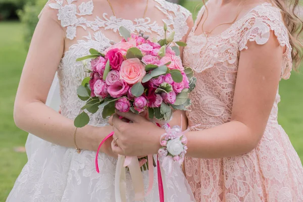 bride with bridesmaid and wedding bouquet in the park