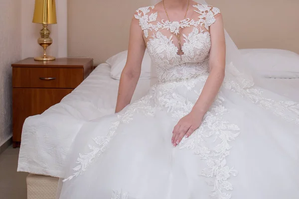 De bruid in een trouwjurk zit in de kamer op het bed — Stockfoto