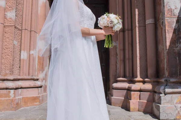 Noiva com buquê de casamento e véu perto da igreja — Fotografia de Stock