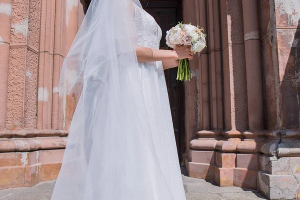 Braut mit Brautstrauß und Schleier in der Nähe der Kirche — Stockfoto
