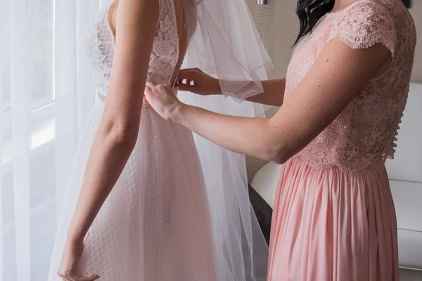 Koszorúslány egy rózsaszín ruhát helyez egy súlytalan esküvői ruha — Stock Fotó