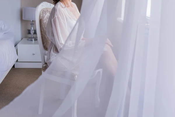 Bruden sitter på en stol klädd i en peignoir — Stockfoto