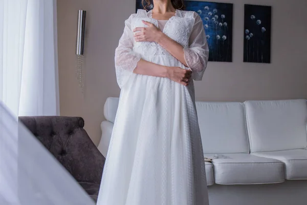 Bride in peignoir holding a wedding dress — Stock Photo, Image
