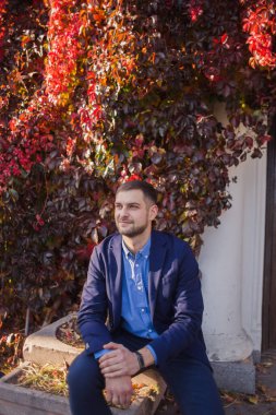 Takım elbiseli bir adam klasik binanın yanında oturuyor.