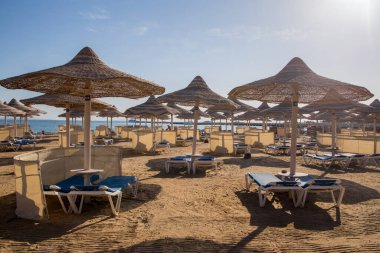 Kumlu plaj güneşliği ve sazdan şemsiyeler.