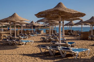 Kumlu plaj güneşliği ve sazdan şemsiyeler.