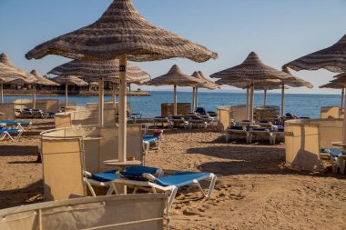 Kumlu plaj güneşliği ve sazdan şemsiyeler.