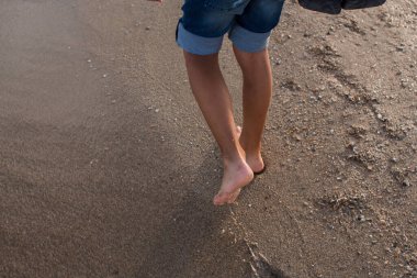 Çocuk kumlu sahil boyunca yürüyor.