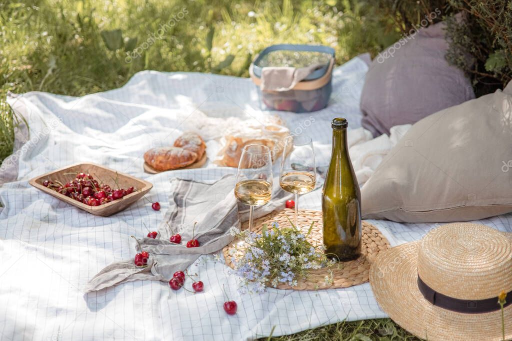 Aesthetic picnic outdoors with wine glasses bread berries and flowers. Rustic picnic with neutral tones colours. 