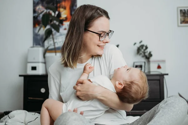 Anne, küçük bebeğiyle ev hayatı konseptinde oynuyor. Tarafsız beyaz kıyafetler, cinsiyet ayrımı olmayan renkler.