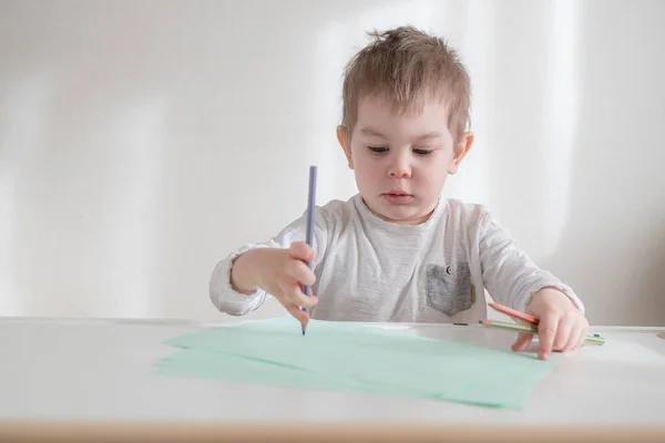 Kleine peuter jongen tekening op neutrale witte achtergrond thuis. — Stockfoto