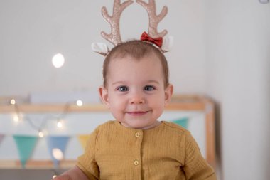 Saç bandı boynuzları olan küçük bir kız çocuk odasında Noel ışıklarıyla bekliyor. Noel tatili ilham.