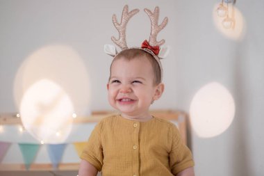 Saç bandı boynuzları olan küçük bir kız çocuk odasında Noel ışıklarıyla bekliyor. Noel tatili ilham.