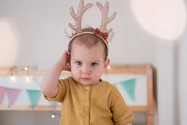 Saç bandı boynuzları olan küçük bir kız çocuk odasında Noel ışıklarıyla bekliyor. Noel tatili ilham.