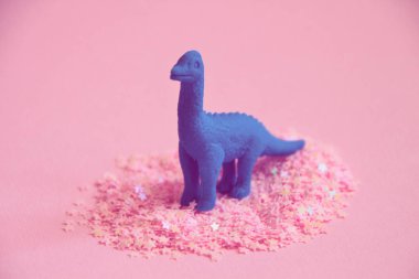 Pembe parti pırıltılar içinde ayakta dinozor figürü.