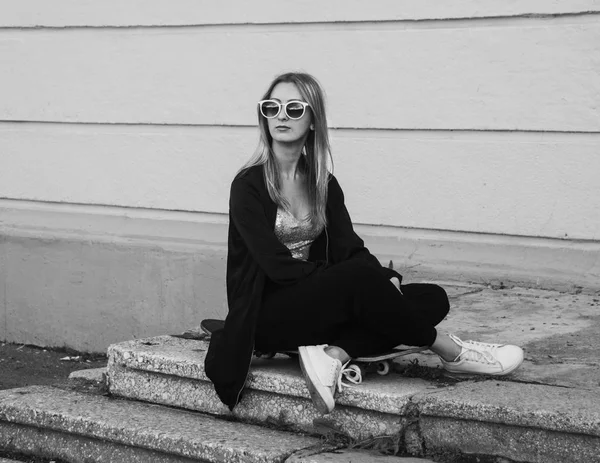 Mujer de moda sentada en el monopatín. Chica en gafas de sol con longboard en las escaleras. Foto en blanco y negro —  Fotos de Stock