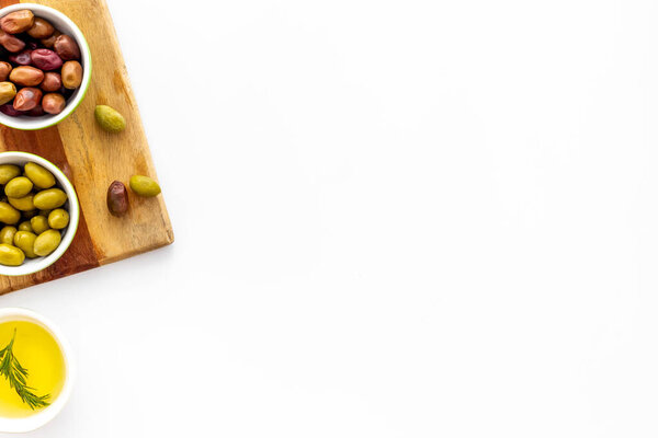 Оливки и оливковое масло в мисках на разделочной доске на белой верхней смотровой площади