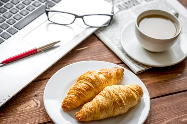 Business lunch with croissant and laptop on wooden desk — Stock Photo, Image