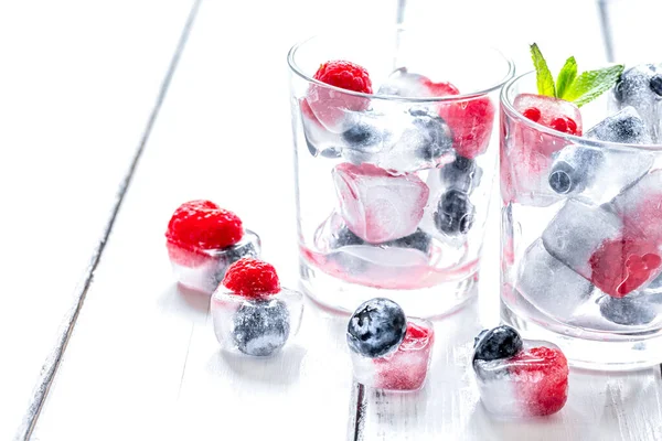 Eiswürfel mit Blaubeere und Himbeere im Glas auf Holztisch — Stockfoto