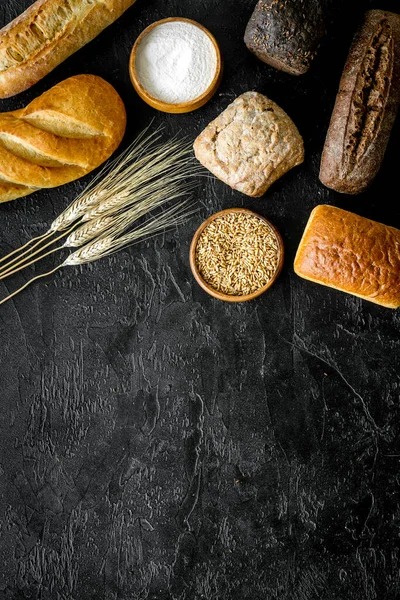 Wholegrain bread near wheat ears on black desk from above space for text — Stock Photo, Image