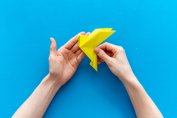 Origami bird in female hands. Care peace concept. Top view