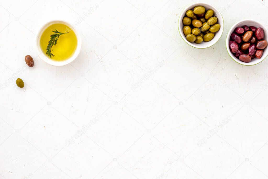 Olive oil in bowl near oilves on white desk from above copy space