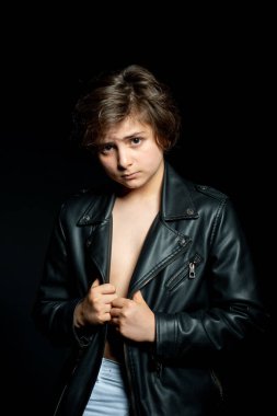 Siyah deri ceketli çocuk siyah arka planda poz veriyor.