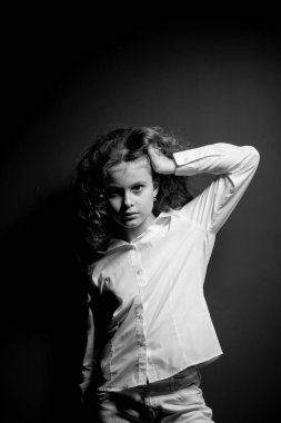 Beyaz tişörtlü, siyah arka planda poz veren ve kameraya bakan sevimli genç kız.