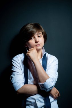 Beyaz gömlekli çocuk siyah arka planda poz veriyor.