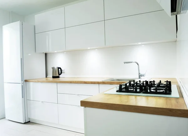 White luxury kitchen view with tools and flowers, modern kitchen tools with white walls, wash basin and gas cooker have attached to the wall, green flower vase on the table, perfect lightning.