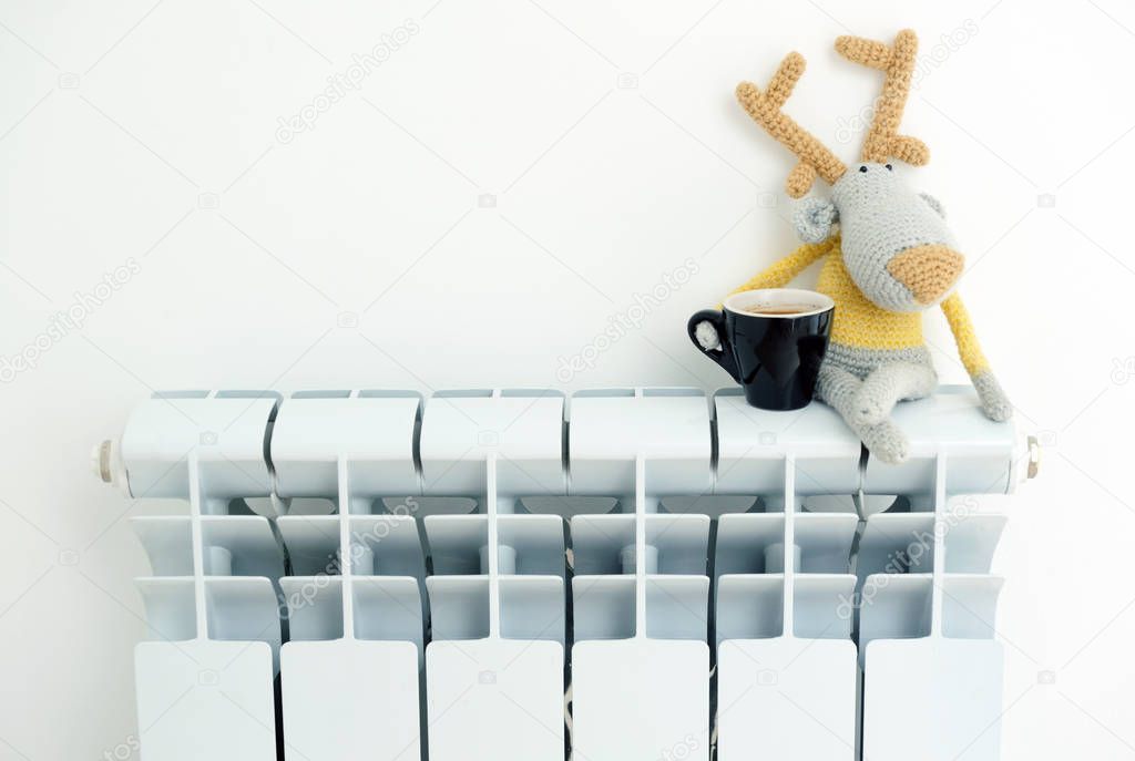 Knitted deer sits on the radiator with a cup in his hand