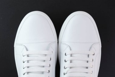 Siyah arka planda bir çift beyaz deri spor ayakkabı. Yukarıdan görüntüle.