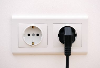 Beyaz arka plan üzerinde beyaz elektrik prizinin takılı siyah elektrik akor