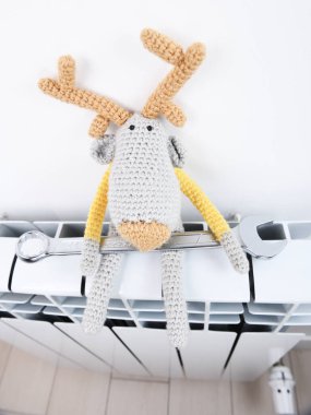 Örgü geyik elinde İngiliz anahtarıyla bir radyatörün üzerinde oturur. Radyatör tamiri. Isıtma sezonu.