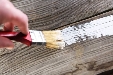 Adam eski ahşap tahtaları fırça ve boyalarla boyuyor, yakın plan.