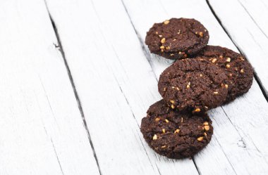 Beyaz odunlu çikolatalı bisküviler. Bir grup kurabiyeye yakın durun. Çikolata parçacıklı, yulaf ezmeli pastırmalı, çerçeveyi beyaz çikolatalı. Kurabiyeler ahşap masada.