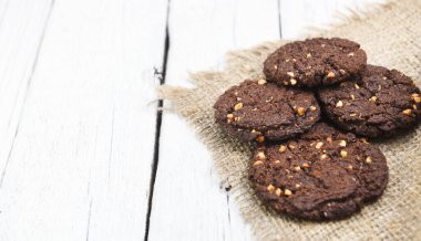 Beyaz odunlu çikolatalı bisküviler. Bir grup kurabiyeye yakın durun. Çikolata parçacıklı, yulaf ezmeli pastırmalı, çerçeveyi beyaz çikolatalı. Kurabiyeler ahşap masada.