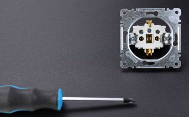 Elektrik İş ve Onarım Maliyetleri. Parçalanmış bir priz siyah arkaplan üzerinde bir tornavida yanında yatar..