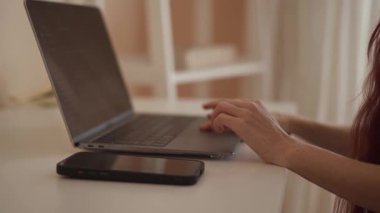 Düzenli bir çalışma alanındaki gösterişli bir dizüstü bilgisayarda çalışan ellerin kapatılması, verimliliği ve modern teknolojiyi ön plana çıkarmak, geliştirilmiş çoklu görev ve odaklanma için yakınlarda bir akıllı telefon bulunması