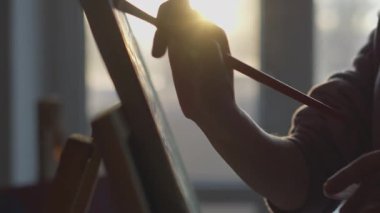 Görüntü, sanatsal süreçteki huzur, sükunet ve tutkuyu vurgulayan sıcak güneş ışığıyla yıkanmış bir tuvale ustalıkla yapılmış bir el resminin yakın çekimini açıkça gösteriyor.