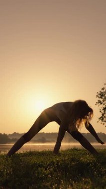 Gün doğumunda huzurlu ve huzurlu bir yoga seansı sergileniyor, sakin suların bulunduğu sakin bir yerde zarif bir şekilde yan açıyla poz veren bir kadın görülüyor.