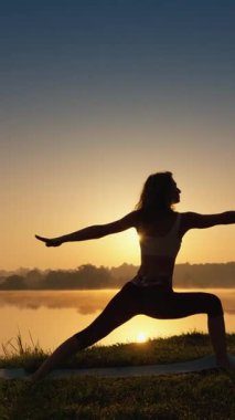 Şafak vakti huzur dolu bir gölün kenarında poz veren, huzurlu bir kadın silueti. Huzur, sağIık ve uyumun özünü yakalıyor. Doğada mükemmel bir denge ve huzur anı.