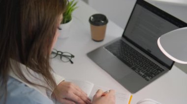 Üretken bir öğrenme ortamında, odaklanmış bir öğrenci, yaratıcı çalışma alanlarını ve konsantrasyonlarını artıran canlı yeşil bir bitki ile kahveyi yudumlarken laptopuna notlar alır.