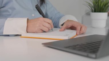 Yakın plan çekimde, minimalist bir çalışma alanında, parlak bir dizüstü bilgisayar ve canlı yeşil bir bitki ile, yaratıcı bir oturumda ilham ve yaratıcılığı somutlaştıran, şık bir not defteri ele alınır.